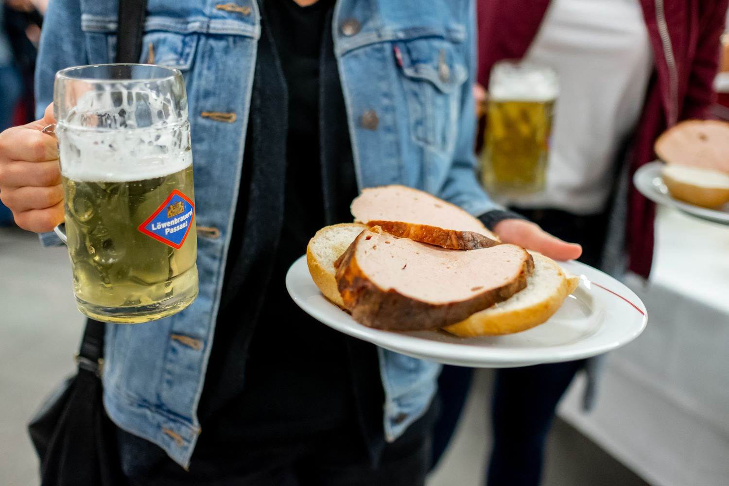 Photo of a person holding a beer in one hand and a Leberkas semmel in this other hand